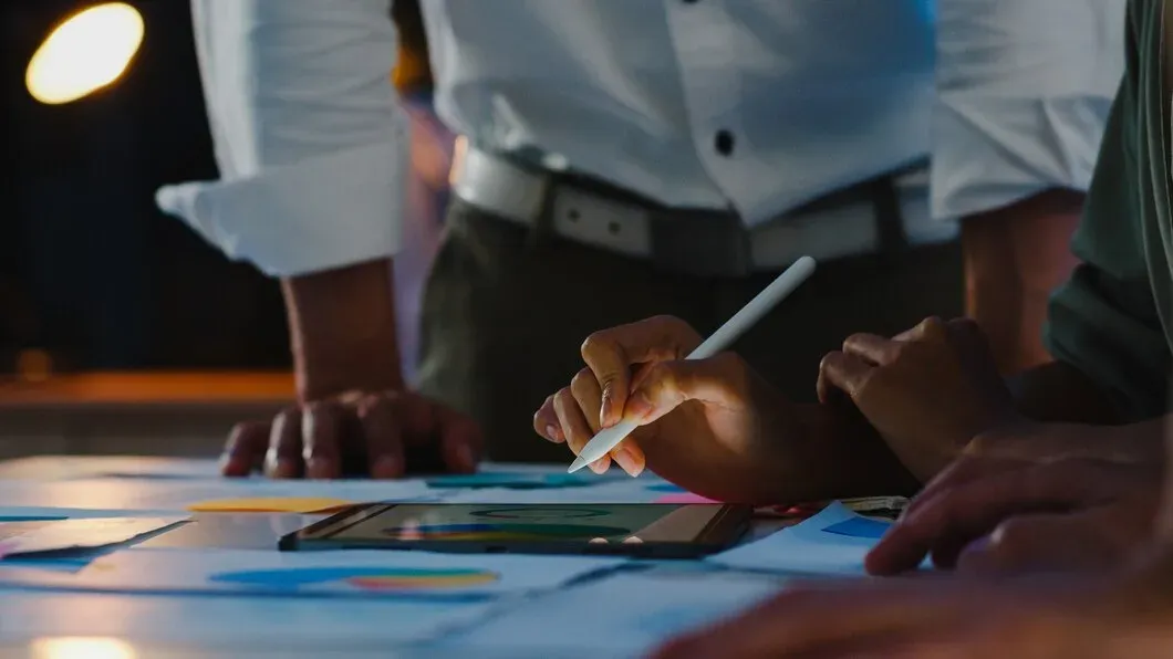 Equipe reunida em volta da mesa analisando gráficos e relatórios de SEO com tablet e caneta digital