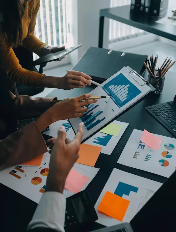 Mãos apontando para gráficos de resultados de SEO impressos sobre uma mesa de trabalho em agência de Joinville
