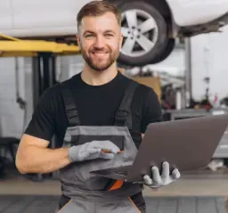 Mecânico sorrindo com um notebook na oficina, que usa site e Google Meu Negócio para atrair clientes em Joinville