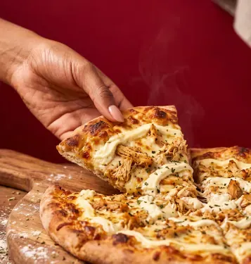 Mão pegando uma fatia de pizza saindo do forno, em uma pizzaria que recebe pedidos e ligações pelo Google Maps