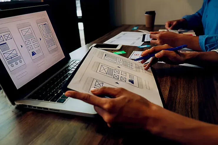 Equipe analisando wireframes de um site em um notebook e em um tablet, na etapa de design do projeto
